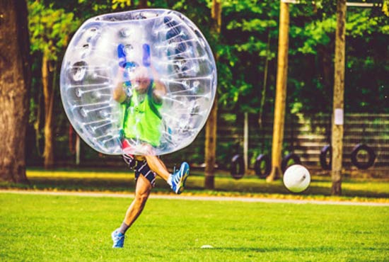 man inside a big inflatable bubble kicking a football ball 